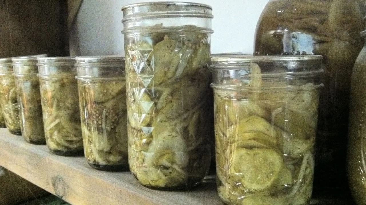 Rows of glass mason jars filled with home-pickled cucumbers and preserved vegetables on a wooden pantry shelf