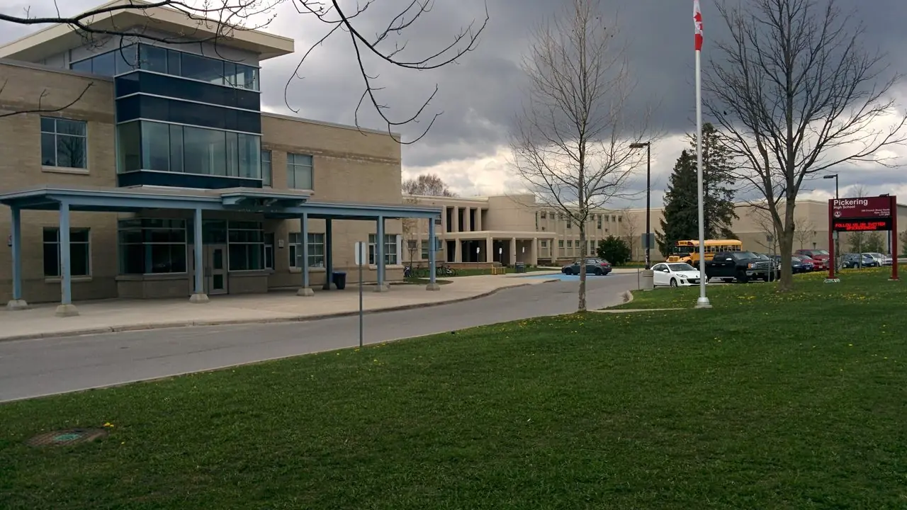 The front entrance of Pickering High School in Ajax, Ontario, with the school sign and a school bus; no people in frame