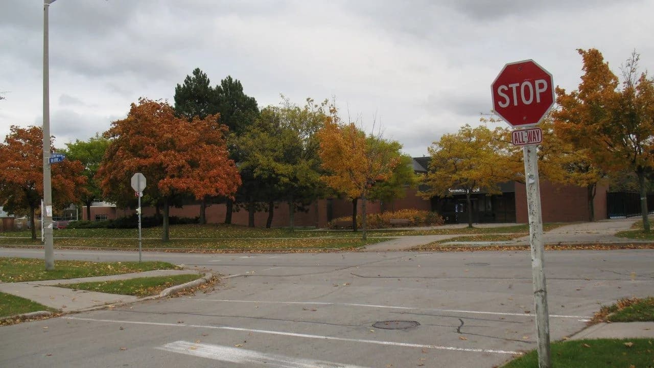 A red stop sign with an all-way tab at a quiet suburban street intersection in autumn; no people visible